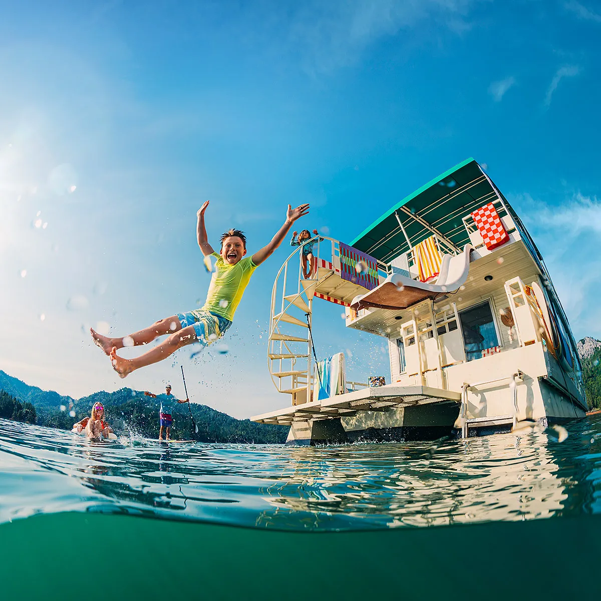 A kid jumps off the diving board on a house boat in the middle of a lake